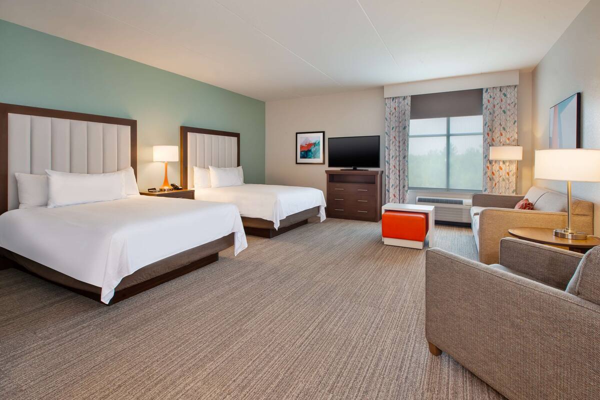 Ein Hotelzimmer mit zwei Betten, einem Fernseher, einem Schreibtisch und einem Sofa.