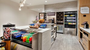 A hotel refreshment area with a chilled beverage dispenser, snack bowls, and a variety of bottled drinks. - Hilton Garden Inn Columbus Easton (Columbus)