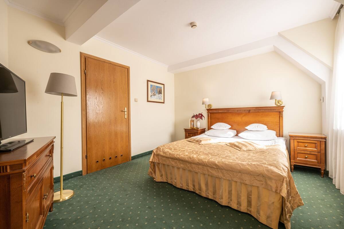 Habitación de hotel con una cama grande, un aparador de madera, un escritorio con lámpara y un cuadro en la pared.