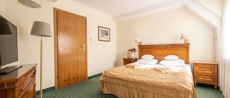 A hotel room with a large bed, a wooden dresser, a desk with a lamp, and a painting on the wall.