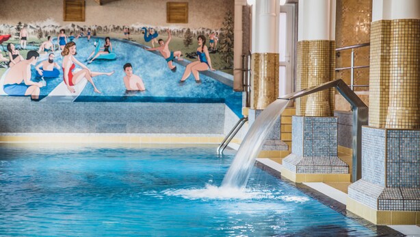A swimming pool with a waterfall feature and a mural depicting people swimming. - Krupówki40 (Zakopane)