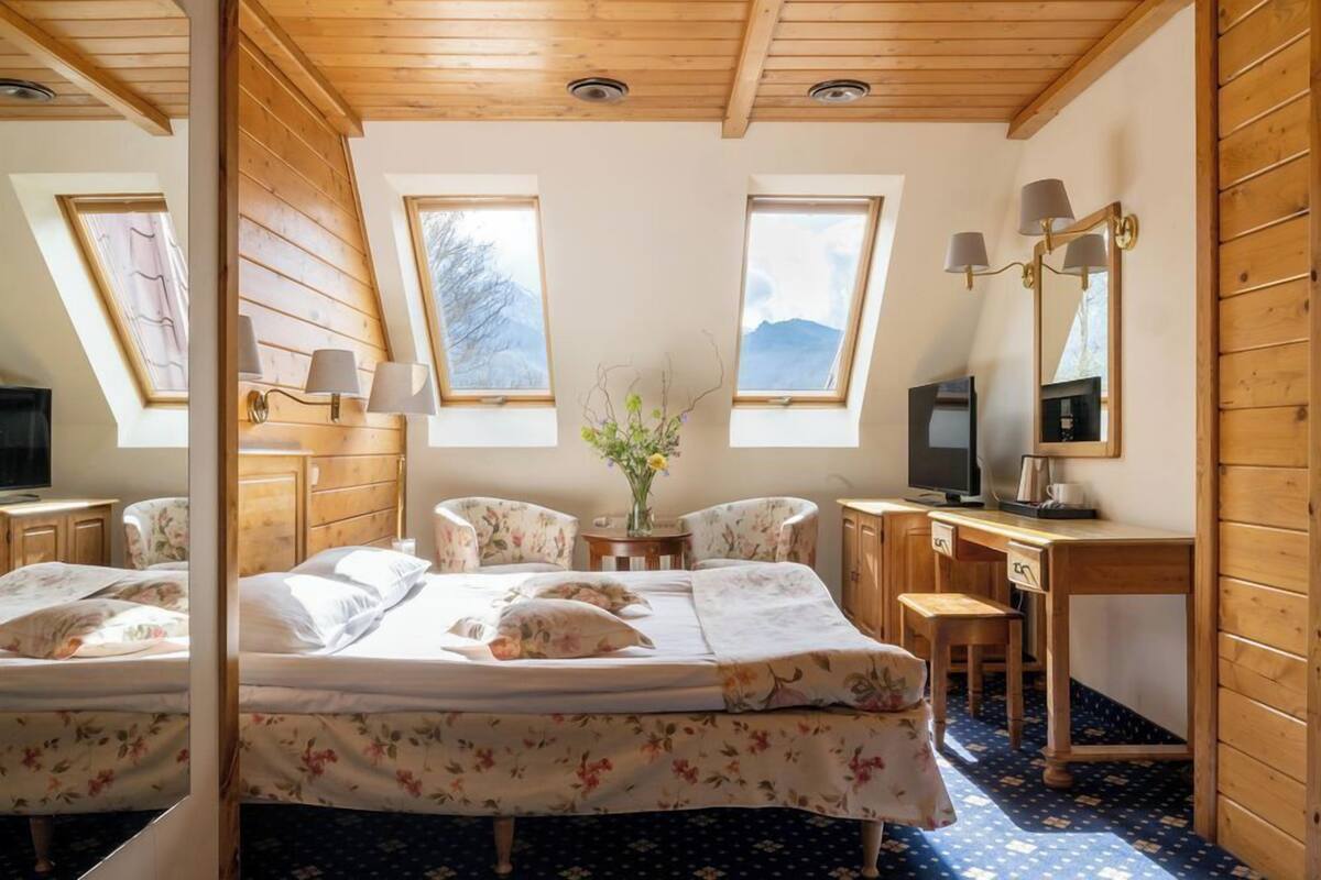 Un dormitorio con cama, dos sillas, un escritorio, un televisor y un espejo.
