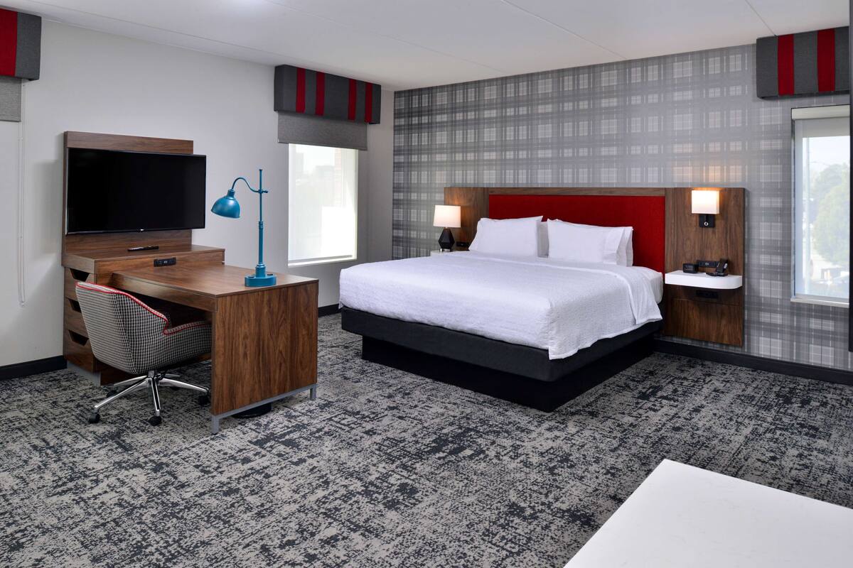 A hotel room with a large bed, a desk with a computer, a TV, and a window.