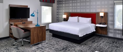 A hotel room with a large bed, a desk with a computer, a TV, and a window.
