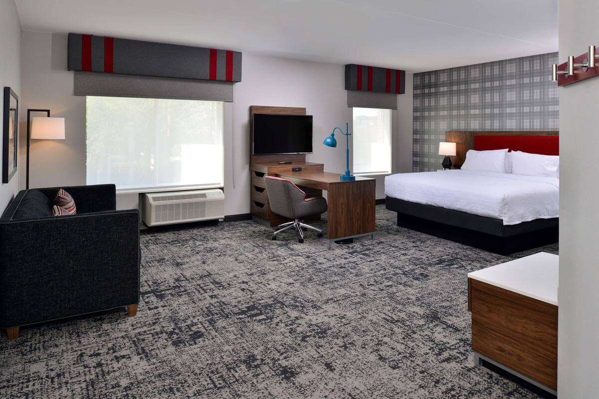 A hotel room with a bed, desk, chair, television, and a radiator.