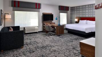 A hotel room with a bed, desk, chair, television, and a radiator.