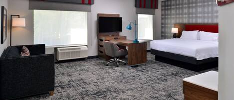 A hotel room with a bed, desk, chair, television, and a radiator.