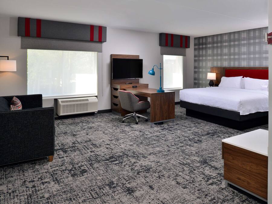A hotel room with a bed, desk, chair, television, and a radiator.