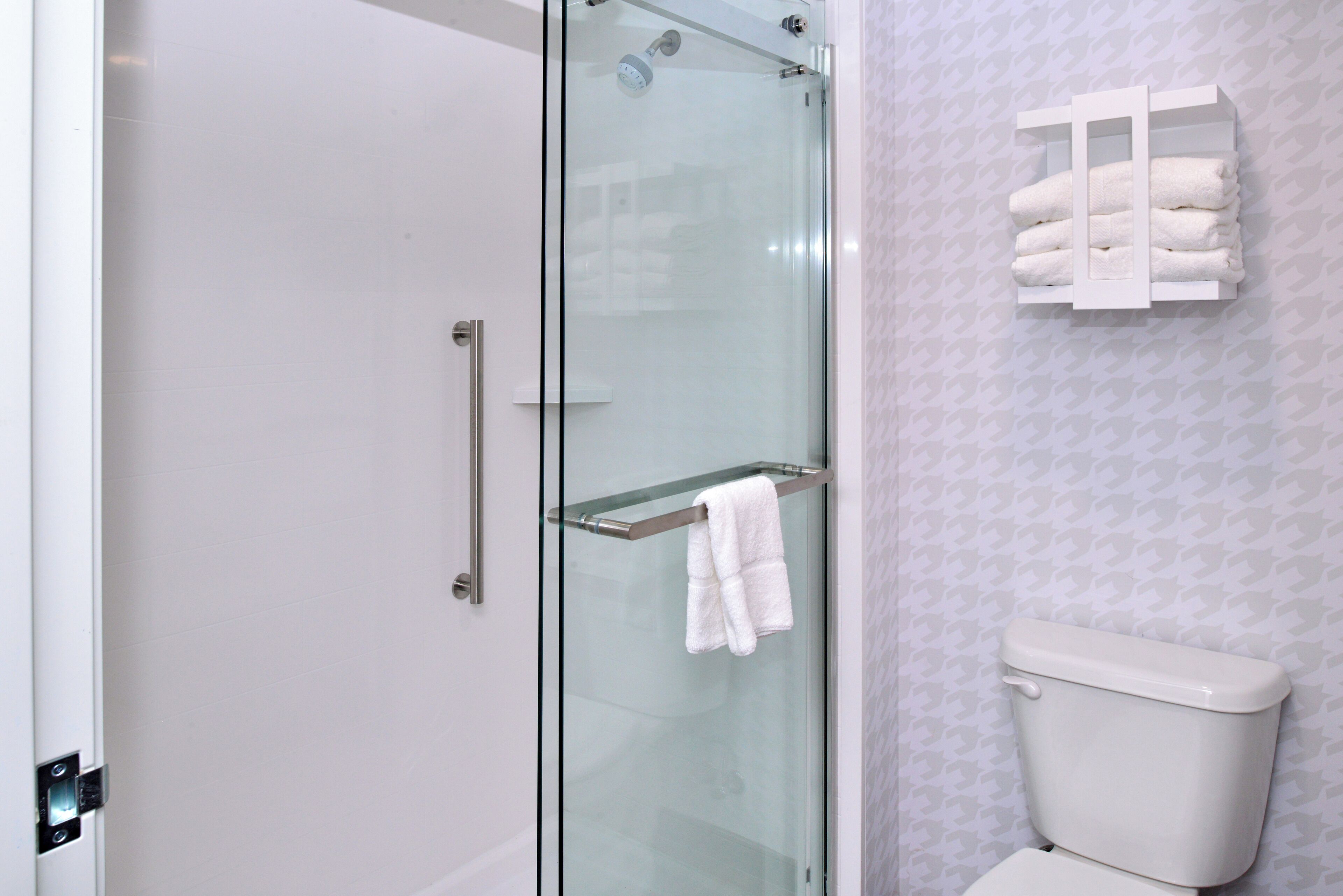 A bathroom with a glass shower enclosure, a glass door, and a towel rack with folded towels.