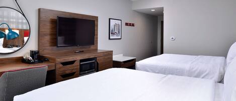 A hotel room with two beds, a flat-screen TV mounted on a wooden panel, a small desk with a coffee maker, and a microwave.