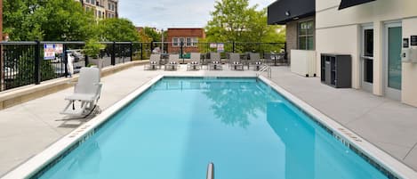 A rectangular pool with a metal handrail, surrounded by white lounge chairs and a black fence.