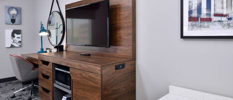 Una habitación moderna con un escritorio de madera, un televisor de pantalla plana, una lámpara de escritorio y un cuadro en la pared.