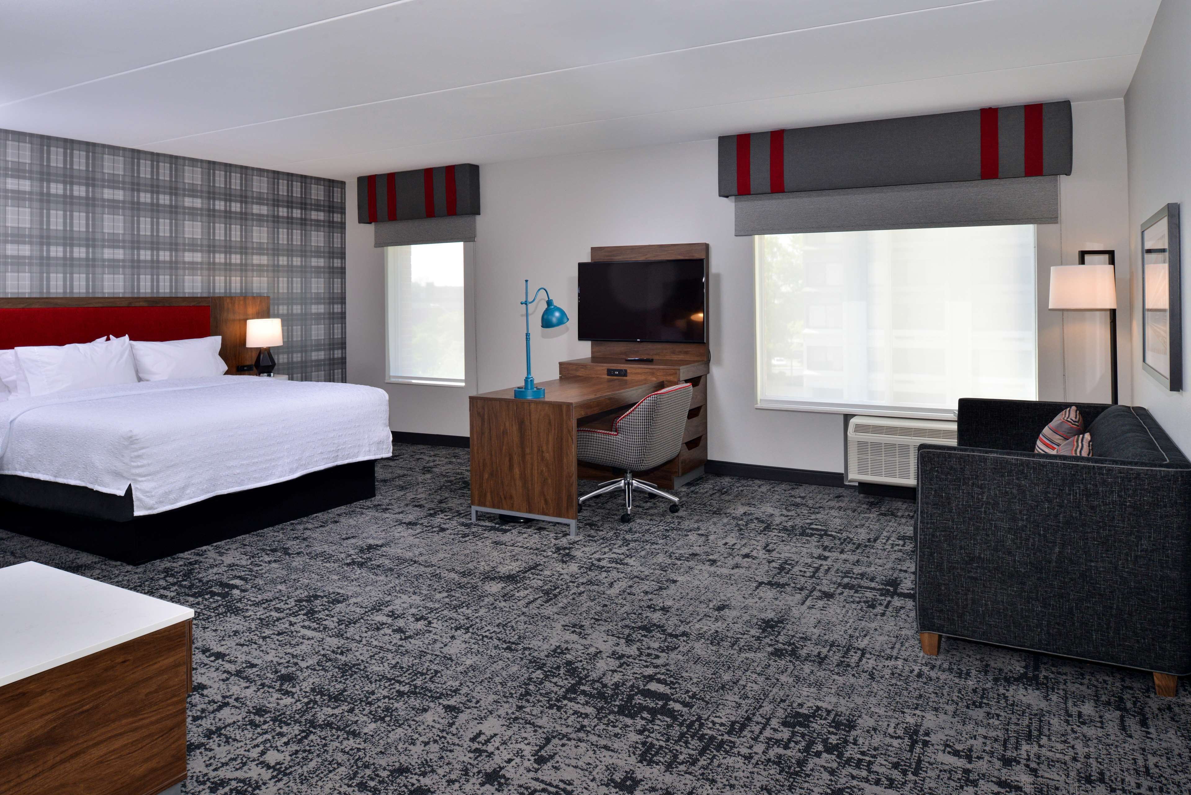 A hotel room with a bed, desk, chair, TV, and large windows.