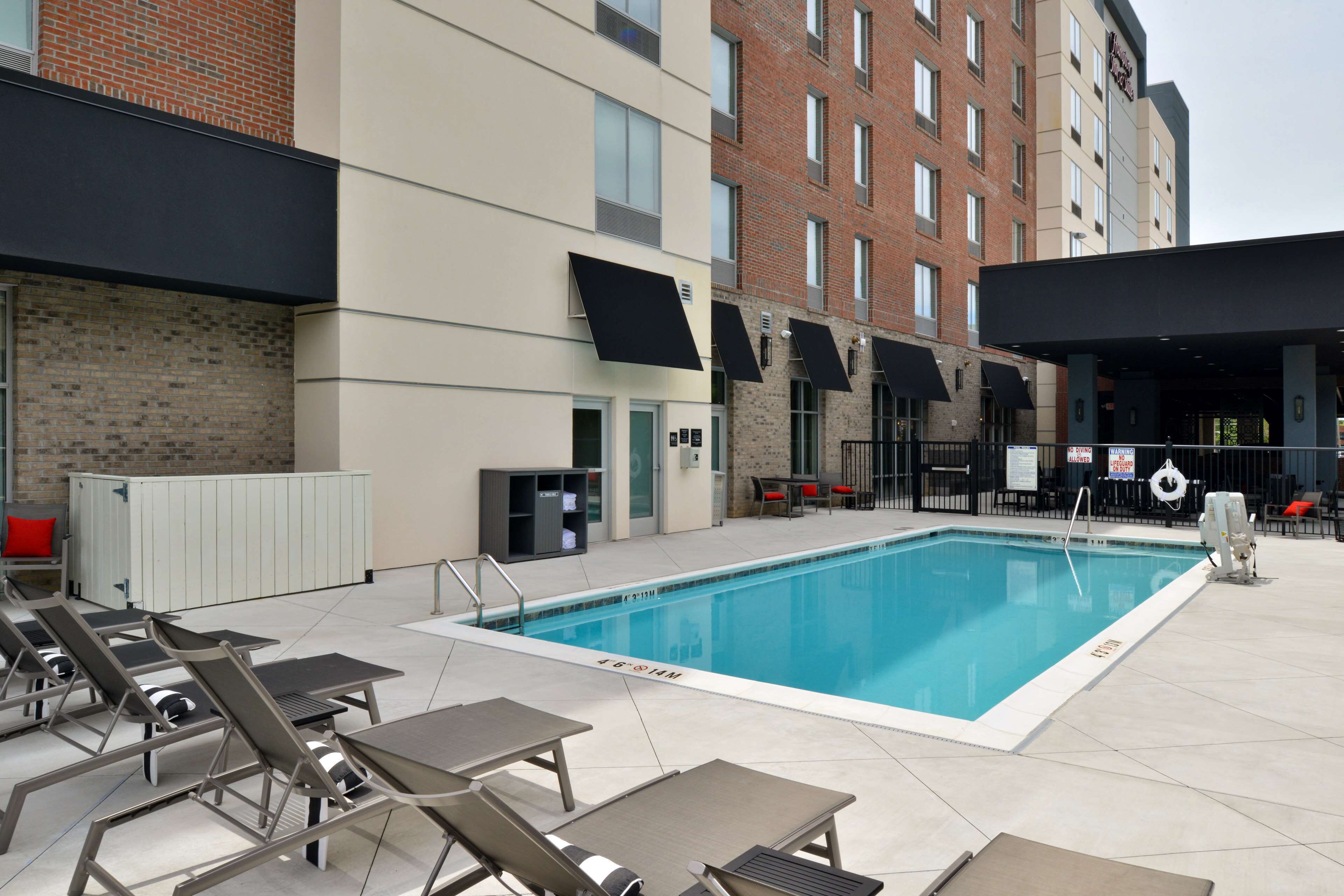 A rooftop pool area with lounge chairs, a pool, and a building with brick and modern design elements.