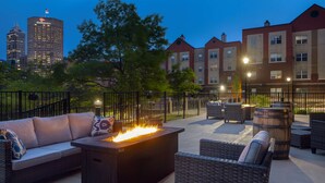 An outdoor patio with a fire feature, wicker furniture, and a view of a city skyline at dusk. - Hampton Inn Indianapolis Downtown IUPUI (Indianapolis)