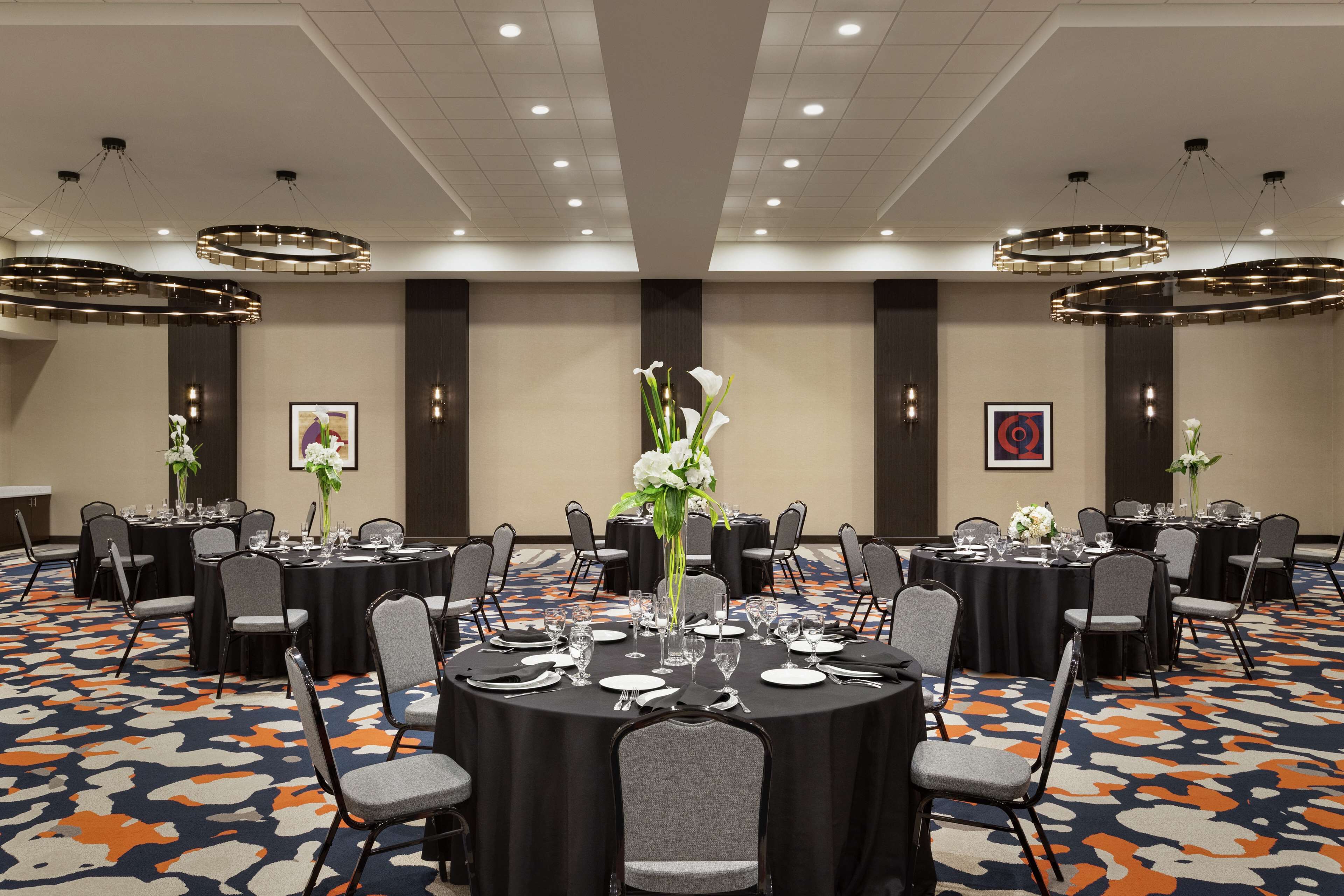 Un salón de conferencias con mesas redondas, sillas y centros de mesa florales.