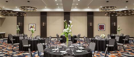 Un salón de conferencias con mesas redondas, sillas y centros de mesa florales.
