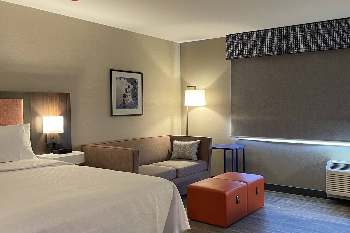 A modern hotel room with a large bed, a sofa, a small table, and a window with a view.