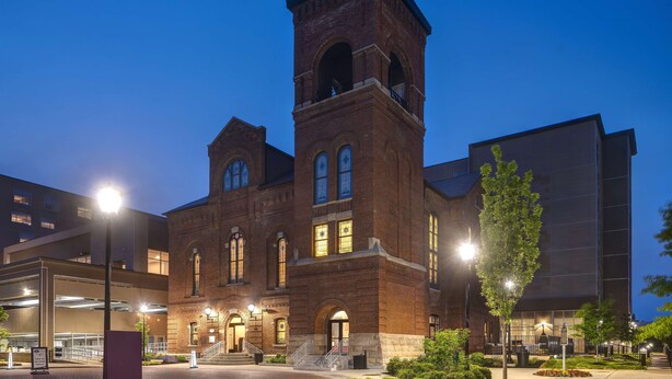 A large brick building with a prominent tower and arched windows, surrounded by modern structures and well-lit pathways. - Hampton Inn Indianapolis Downtown IUPUI (Indianapolis)
