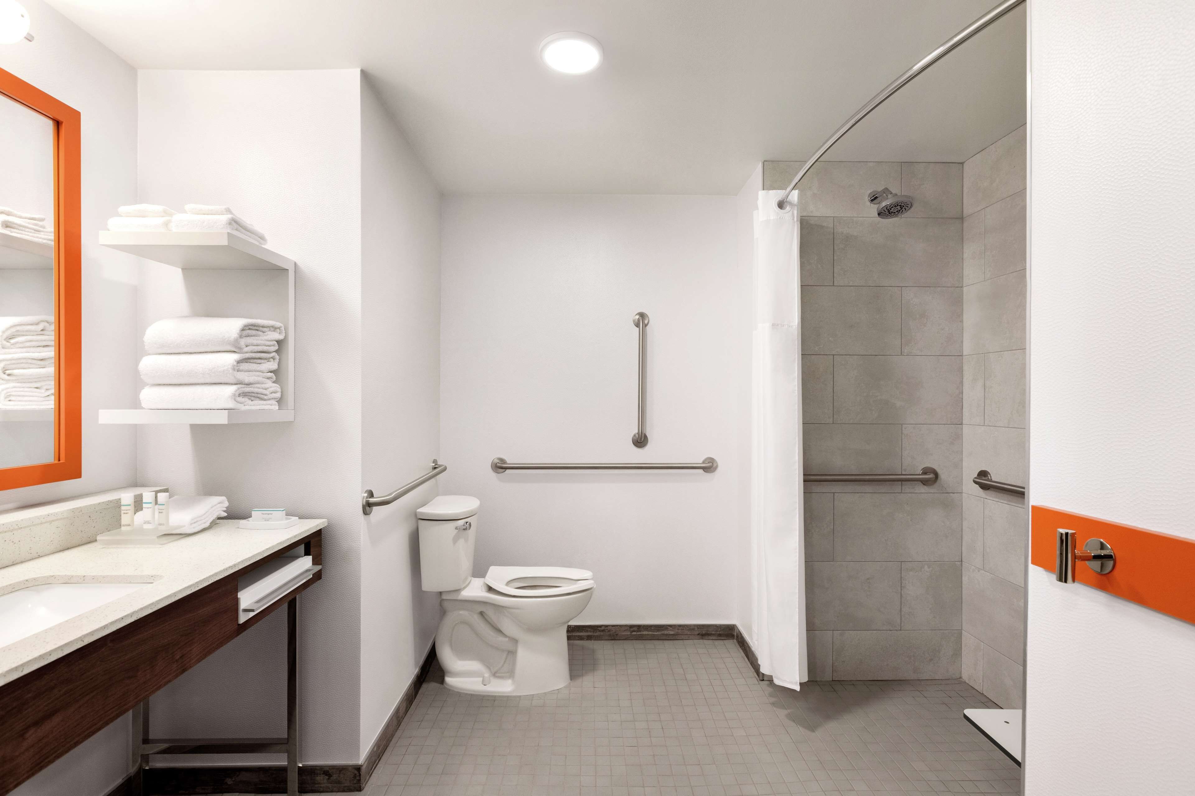 A modern bathroom with a toilet, sink, and shower area, including grab bars for accessibility.