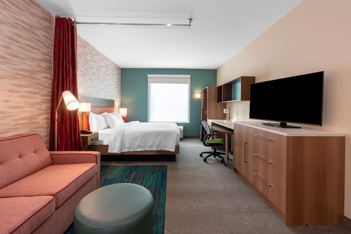 Een hotelkamer met een bed, bureau, televisie, bank en raam.