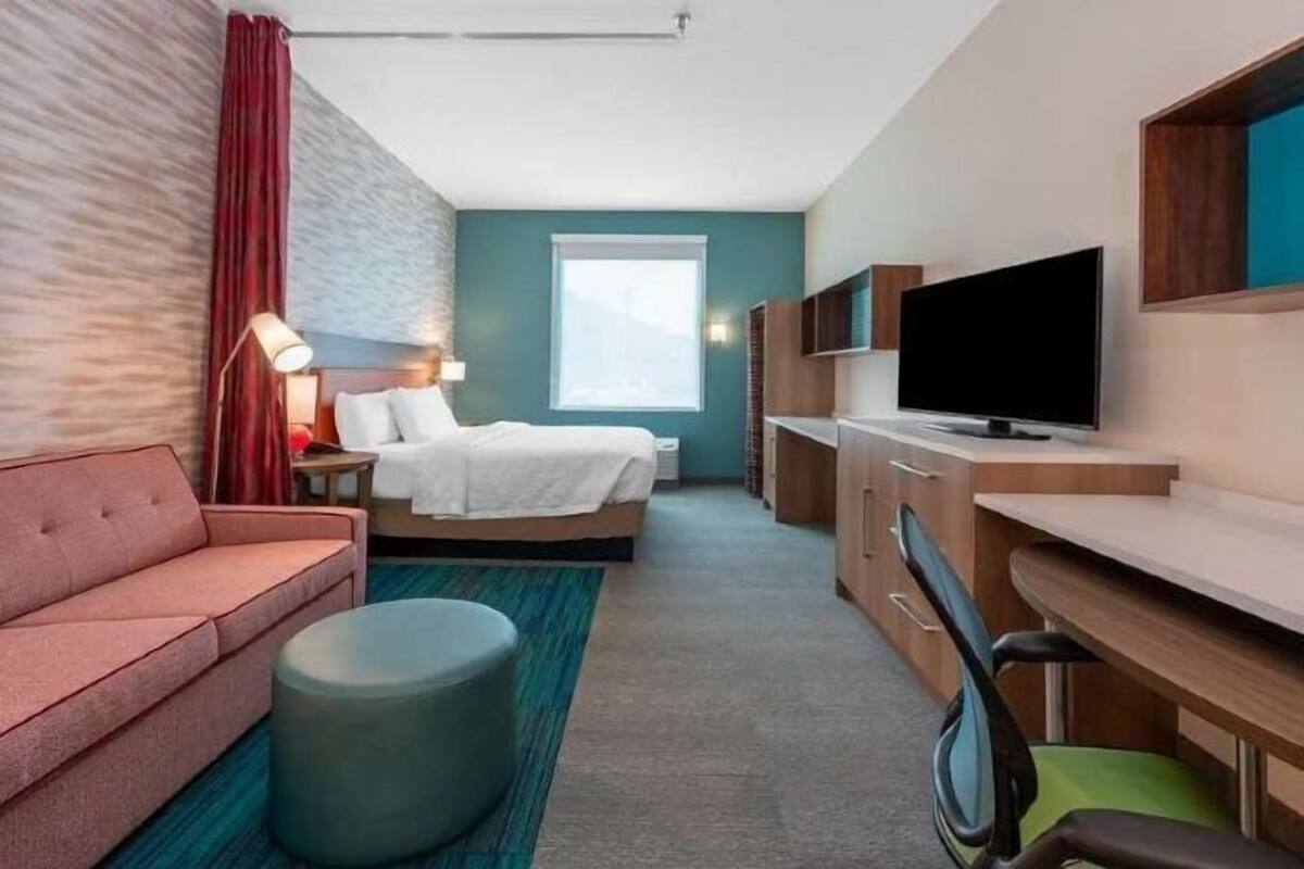 Una habitación de hotel con cama, escritorio, televisor, sofá y ventana.