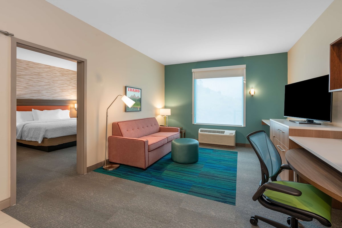Een hotelkamer met een bed, een bank, een bureau, een televisie en een raam.