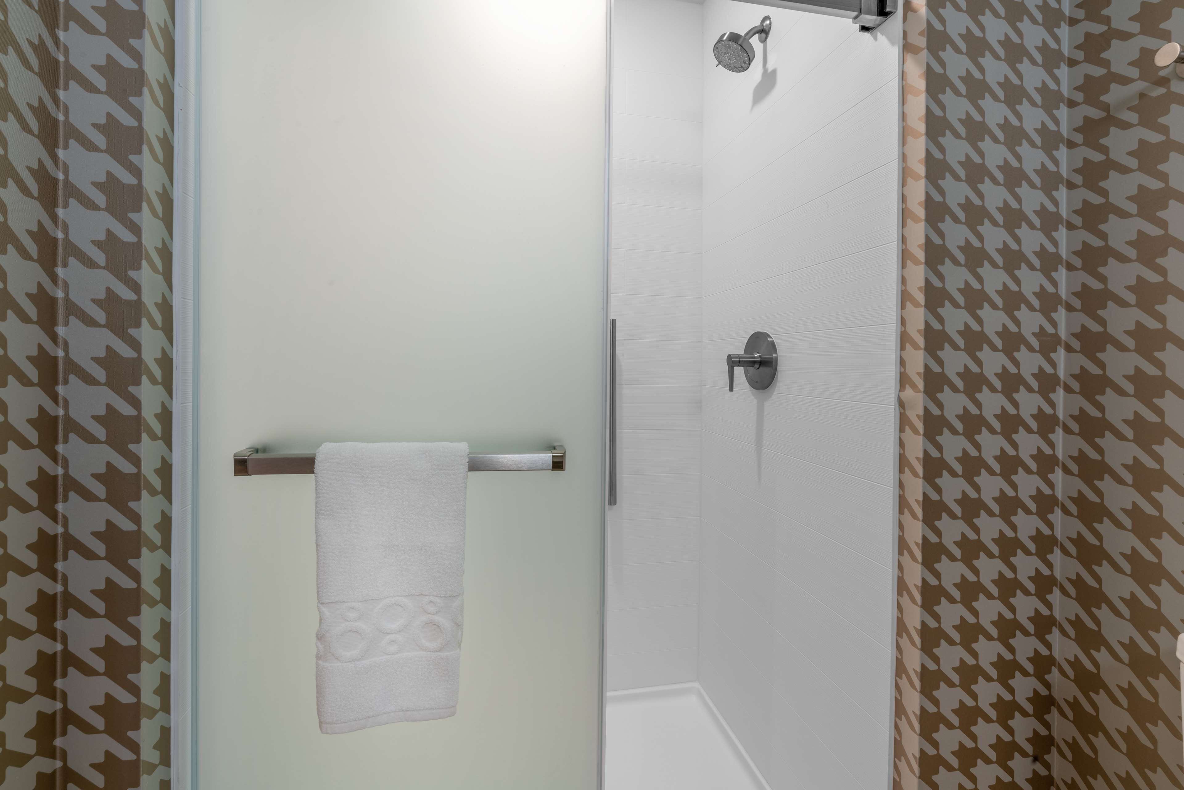 Une salle de bain dotée d’une porte en verre, d ’une serviette suspendue à un porte-serviettes en métal et d’une douche avec un pommeau de douche amovible.