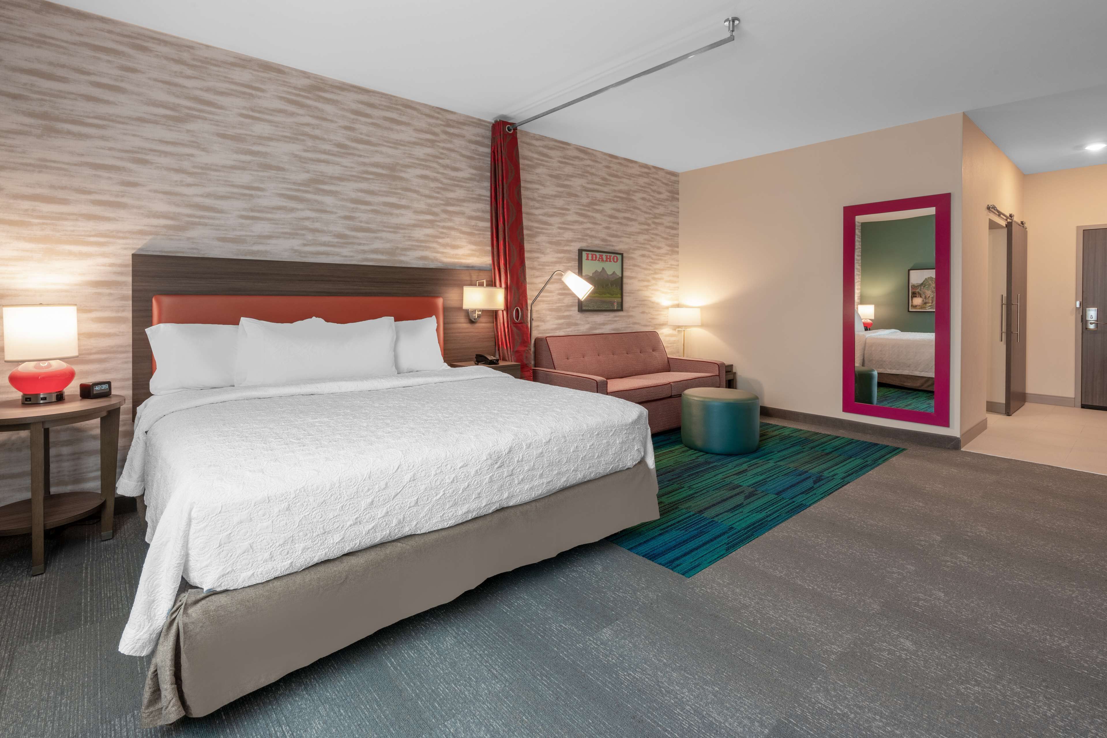 A hotel room with a large bed, a desk with a lamp, a chair, and a small table.
