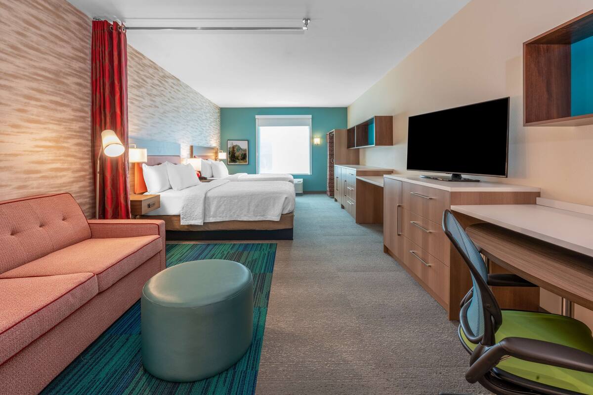 Een hotelkamer met een bed, een bank, een bureau, een stoel, een televisie en een raam.