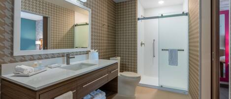 Un baño moderno con un espejo grande, lavamanos dobles, inodoro y ducha con mampara de vidrio.