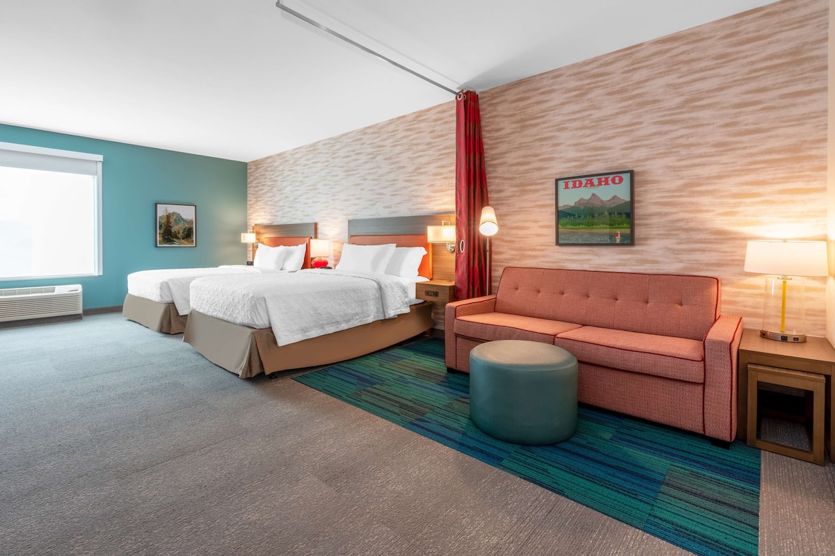 Een hotelkamer met een bed, een bank, een rond poefje, een nachtkastje en een wandlamp.