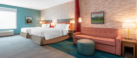 A hotel room with a bed, a sofa, a round ottoman, a nightstand, and a wall-mounted lamp.