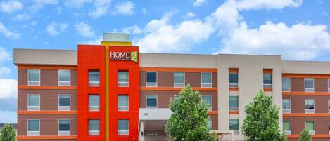 A multi-story hotel with a prominent red and orange facade, numbered 2325, and a parking lot with several cars.
