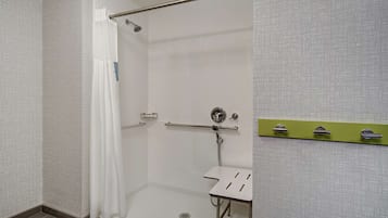 Zona de bany amb cortina de dutxa blanca, barana de sujeció i petit rentaperillos blanc amb penjador verd.
