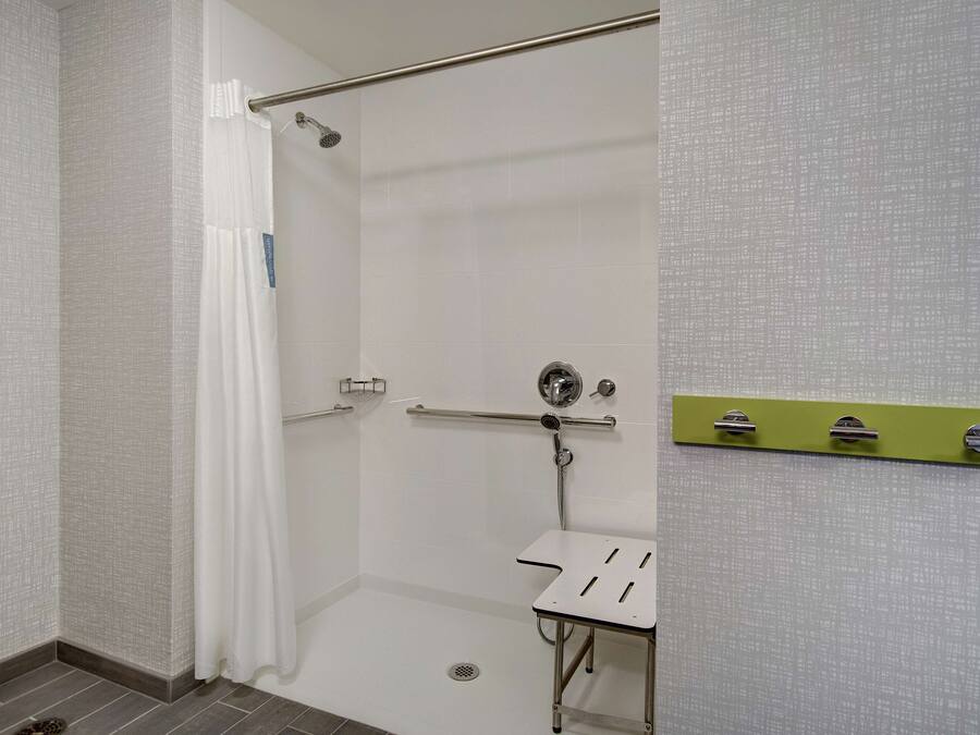 A shower area with a white shower curtain, a grab bar, and a small white sink with a green towel rack.