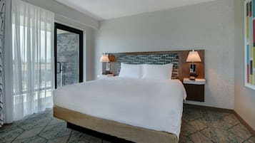 A hotel room with a large bed, two bedside tables with lamps, a stone accent wall, and a view through a glass door.