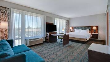 A hotel room with a bed, a desk, a TV, a sofa, and a large window with curtains.