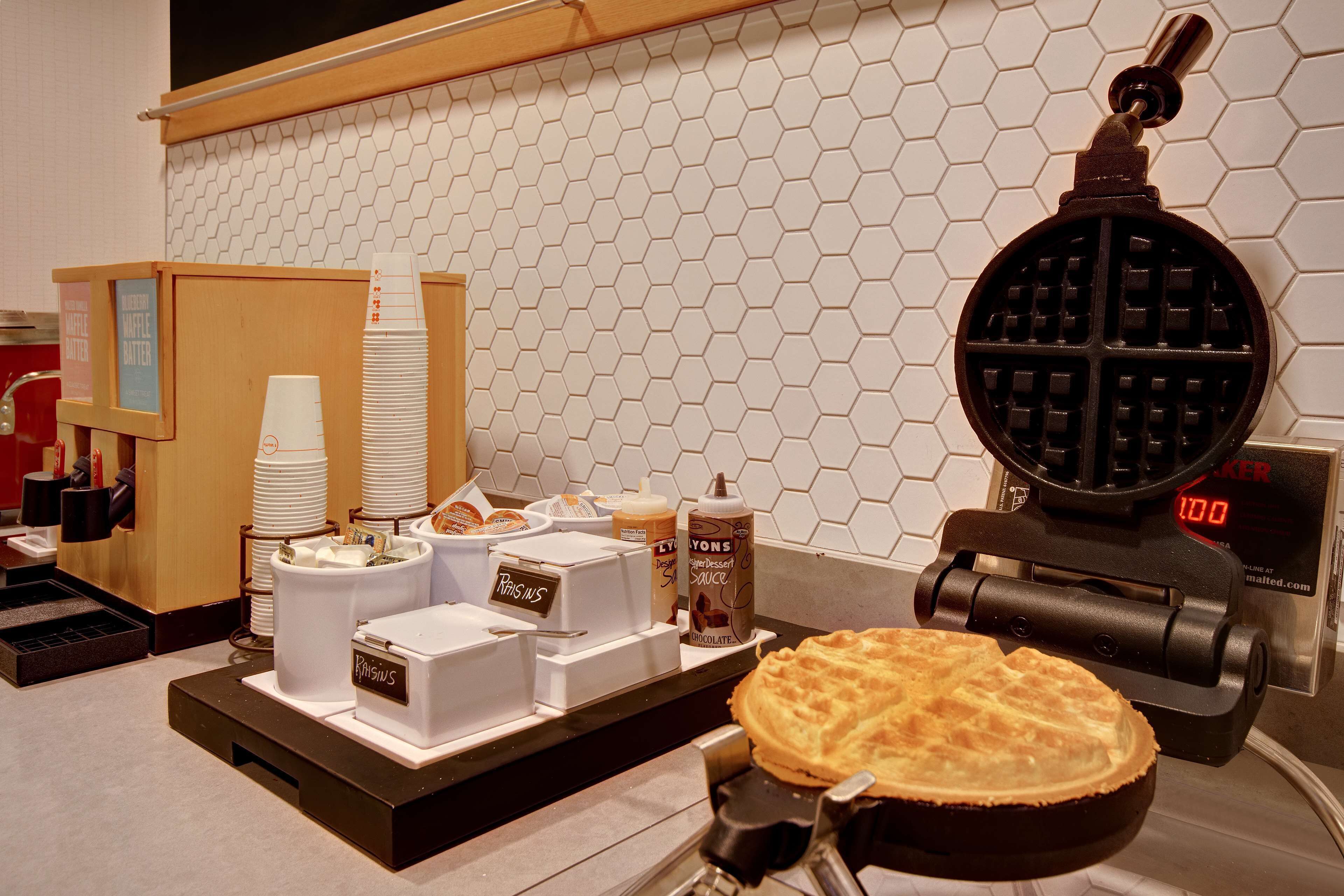 A waffle maker, a waffle, and a coffee machine on a counter.
