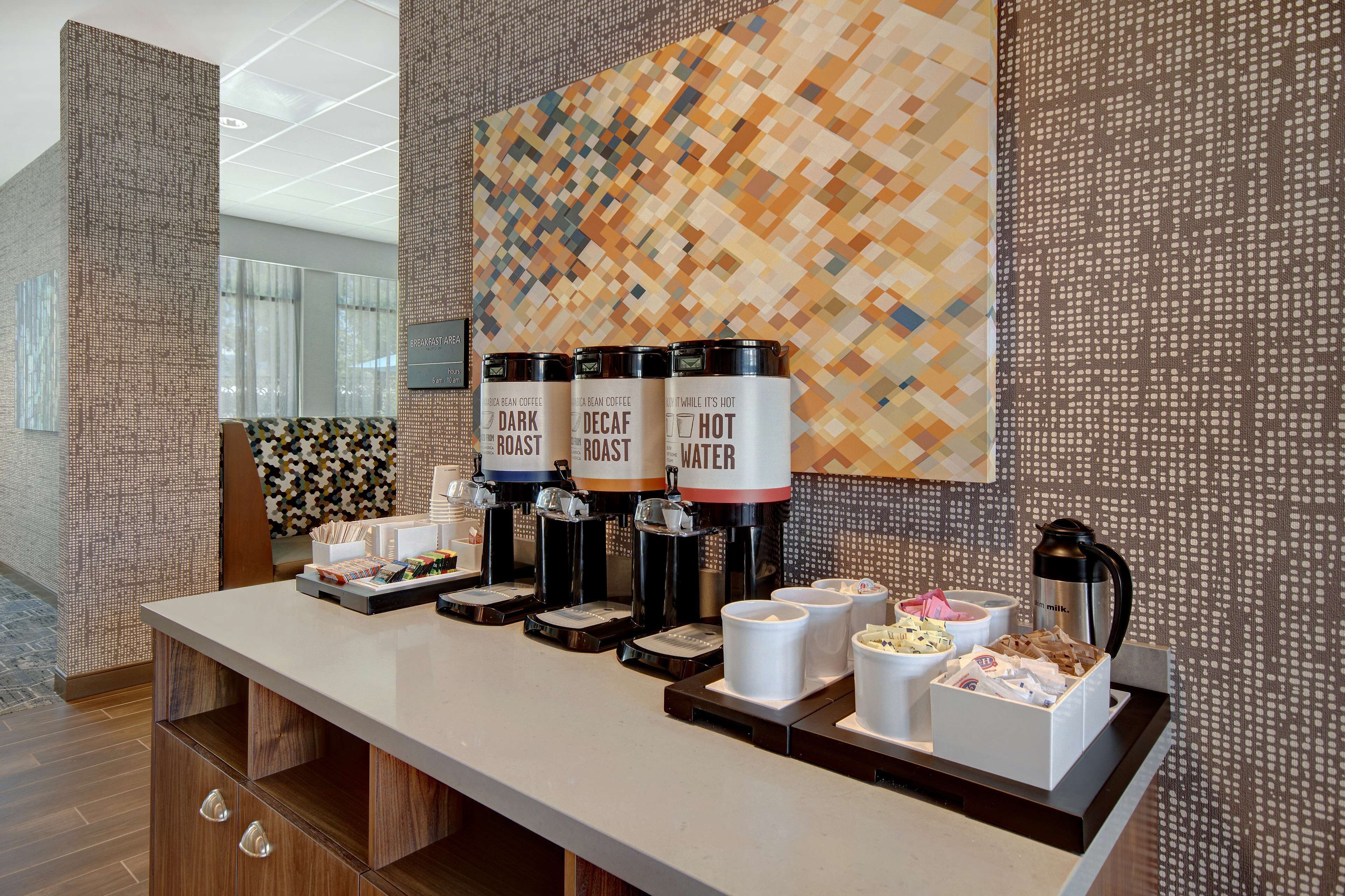 A coffee station with three dispensers labeled 'Dark Roast,' 'Decaf Roast,' and 'Hot Water.' There are also cups and a box of tissues.