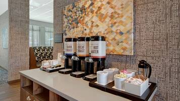 A coffee station with three dispensers labeled 'Dark Roast,' 'Decaf Roast,' and 'Hot Water.' There are also cups and a box of tissues.