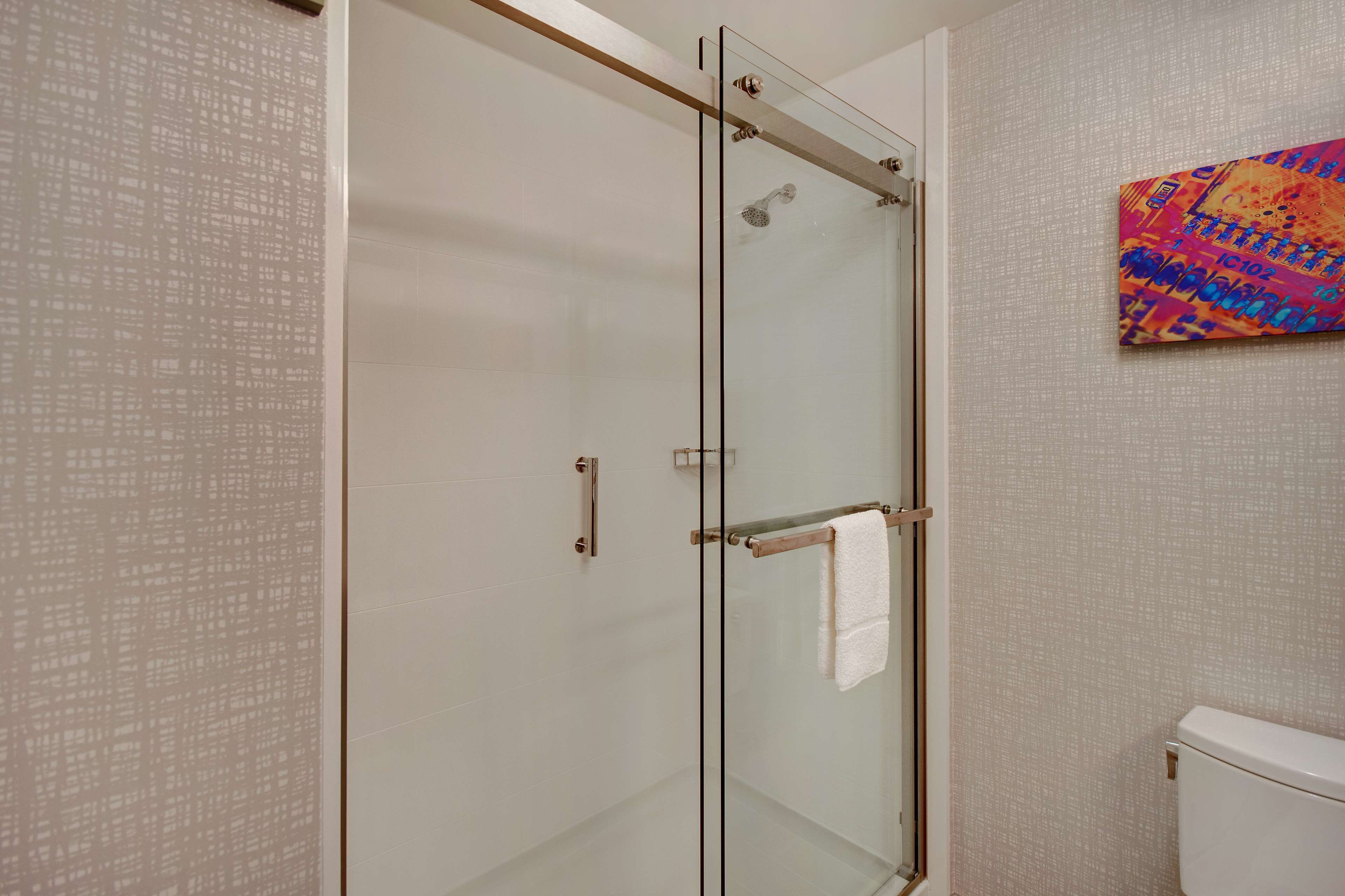 Un baño moderno con cabina de ducha de vidrio, inodoro blanco y un cuadro abstracto de colores en la pared.
