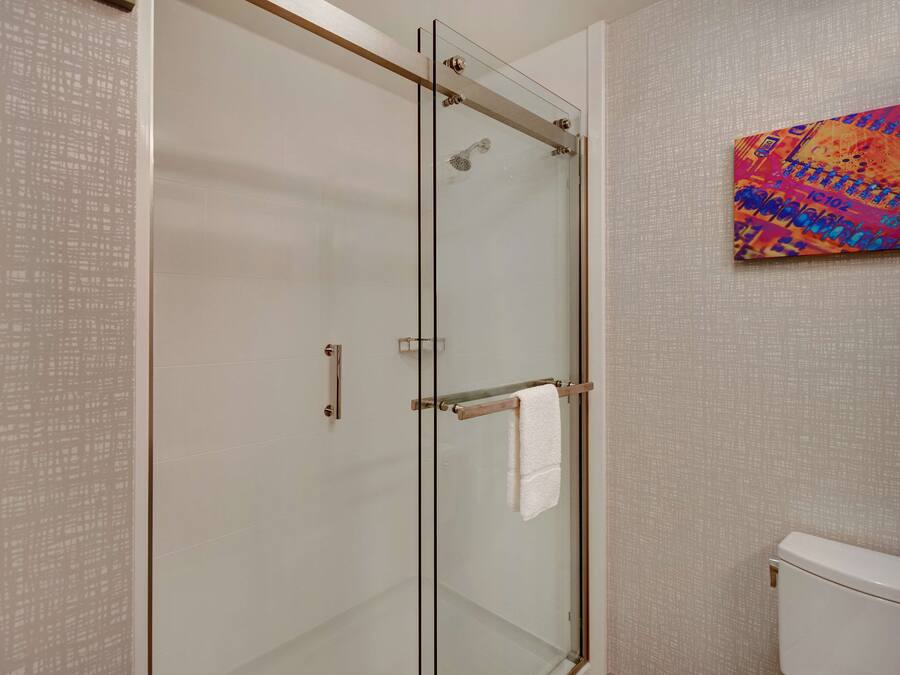 A modern bathroom with a glass shower enclosure, a white toilet, and a colorful abstract painting on the wall.