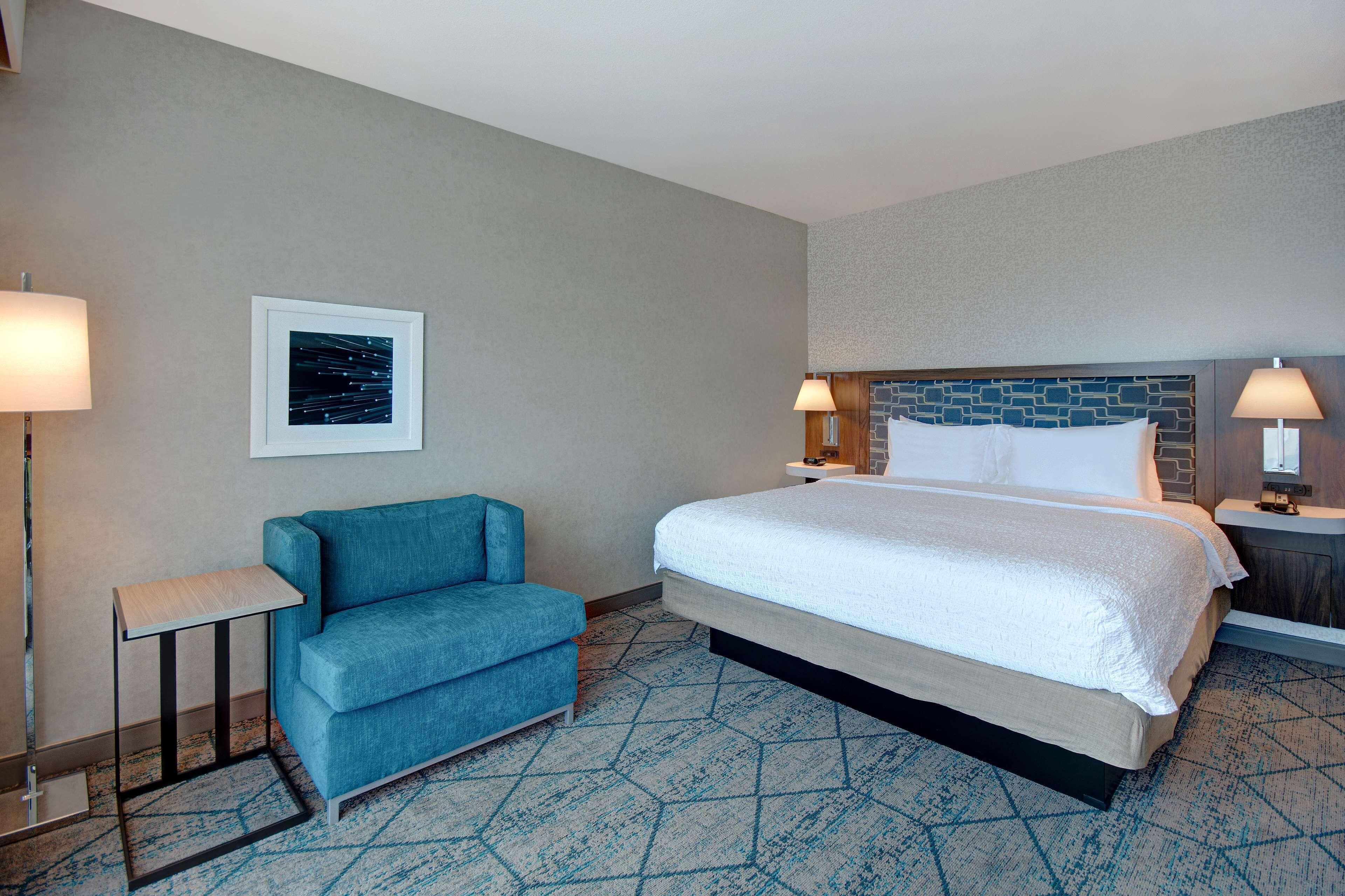 A hotel room with a bed, a blue sofa, a small table, and two bedside lamps.