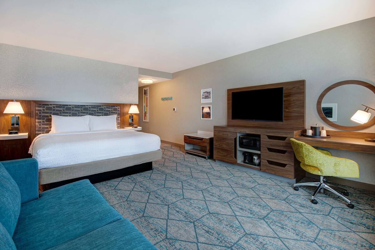 A hotel room with a bed, a desk, a chair, a TV, and a mirror.