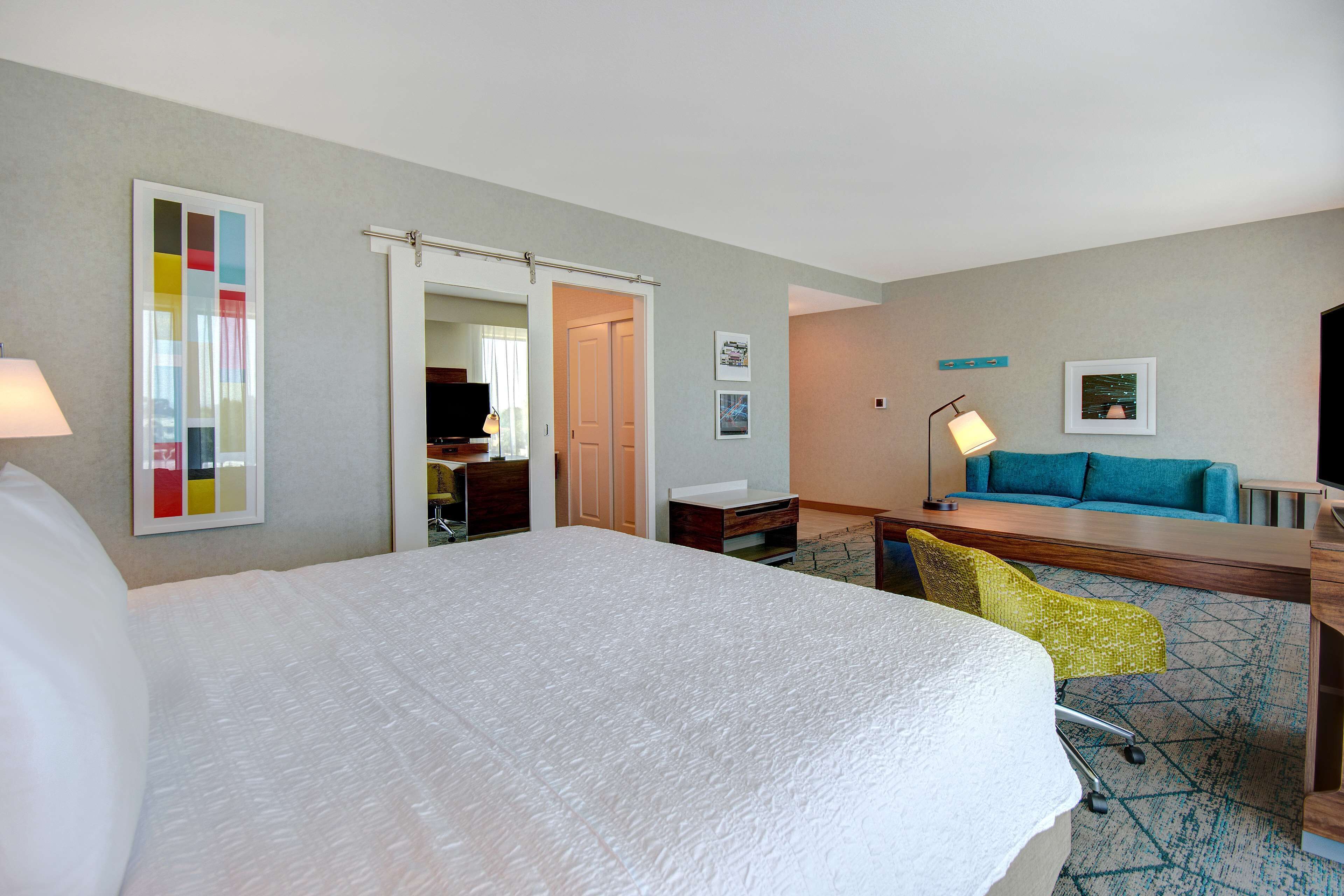 A hotel room with a large bed, a desk with a chair, a sofa, and a TV.