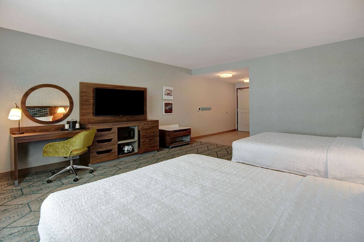 A hotel room with two beds, a desk with a TV, a chair, and a mirror.