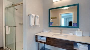 A modern bathroom with a glass shower enclosure, a white sink, and a mirror with a teal frame.