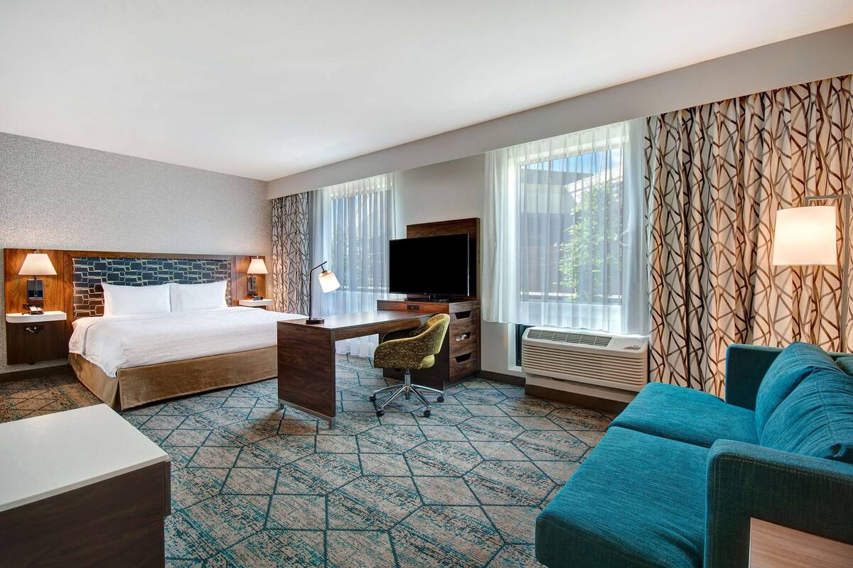 A hotel room with a bed, desk, TV, and a sofa.