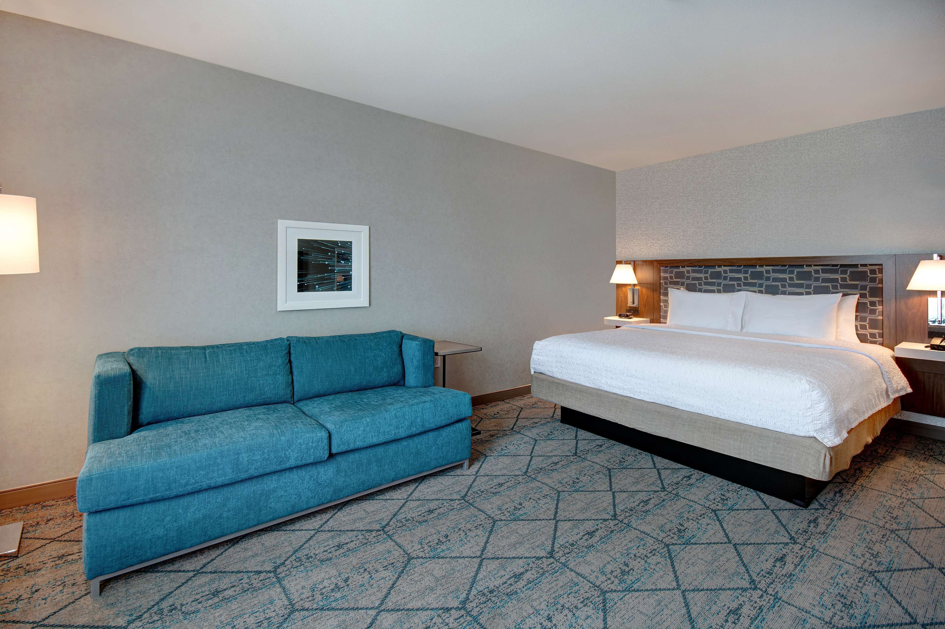 A hotel room with a bed, a blue sofa, a small table, and a wall-mounted picture.